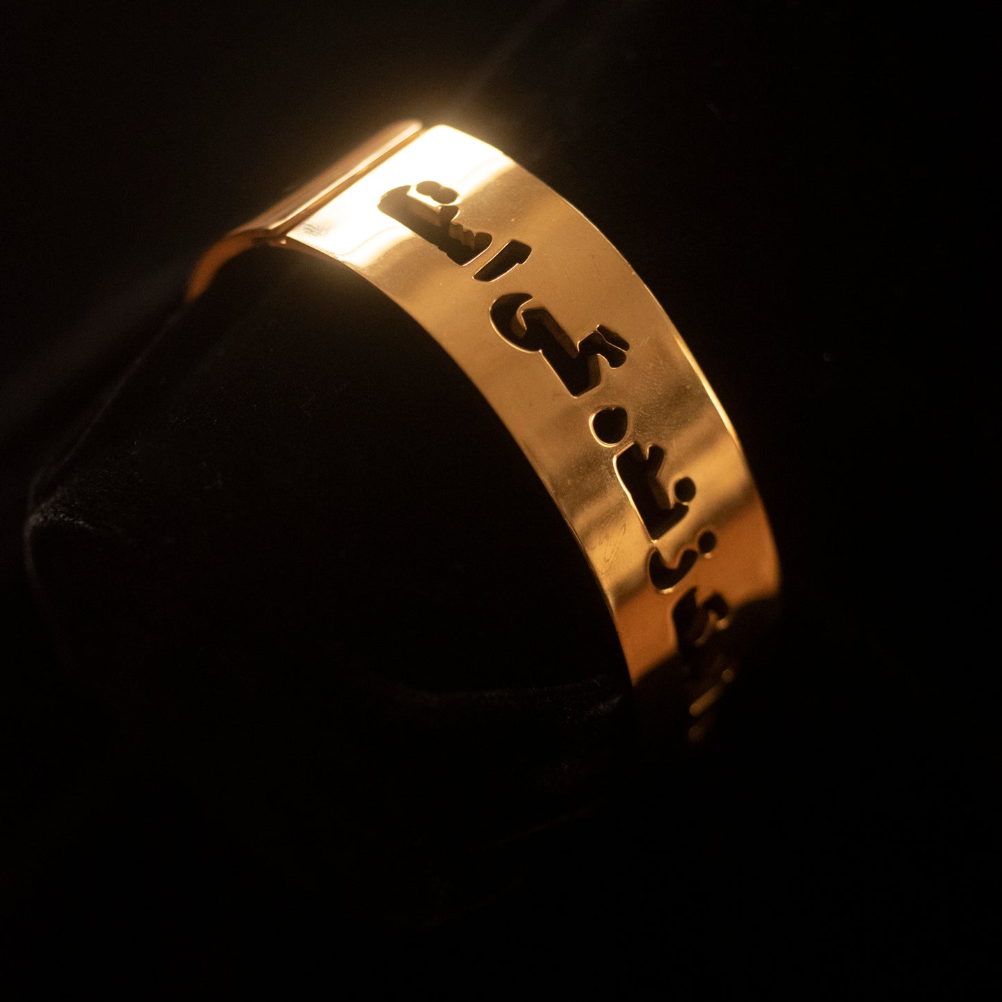 A gold bangle sits on a black backdrop and says Khanda Namak e Zindagi in Dari.