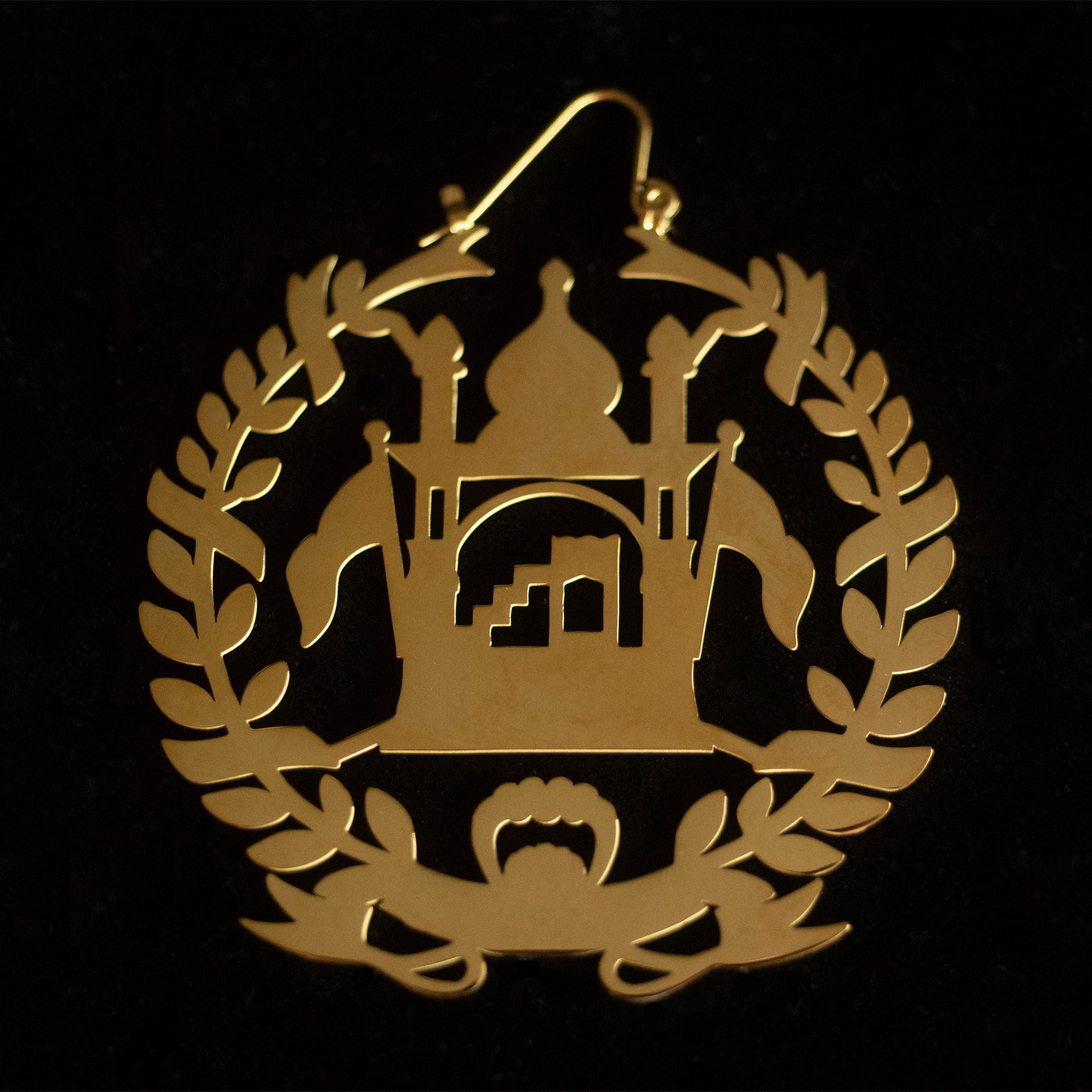 Earrings shaped as the national emblem of Afghanistan in gold against a black background.