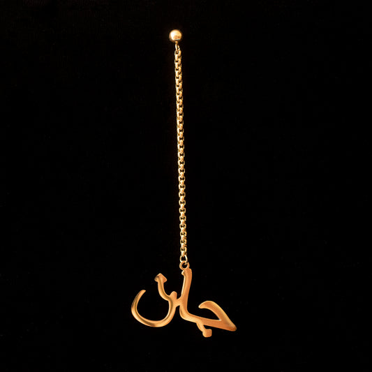 Jaan written in Dari dangly earring in gold against a black backdrop.