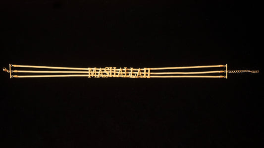 Against a black back drop sits a gold choker chain with the word MASHALLAH written on it.