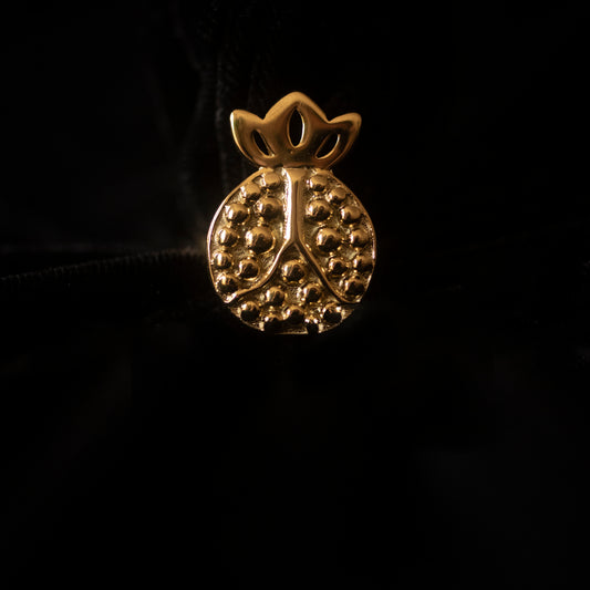 Against a black backdrop sits a pomegranate shaped gold ring. 