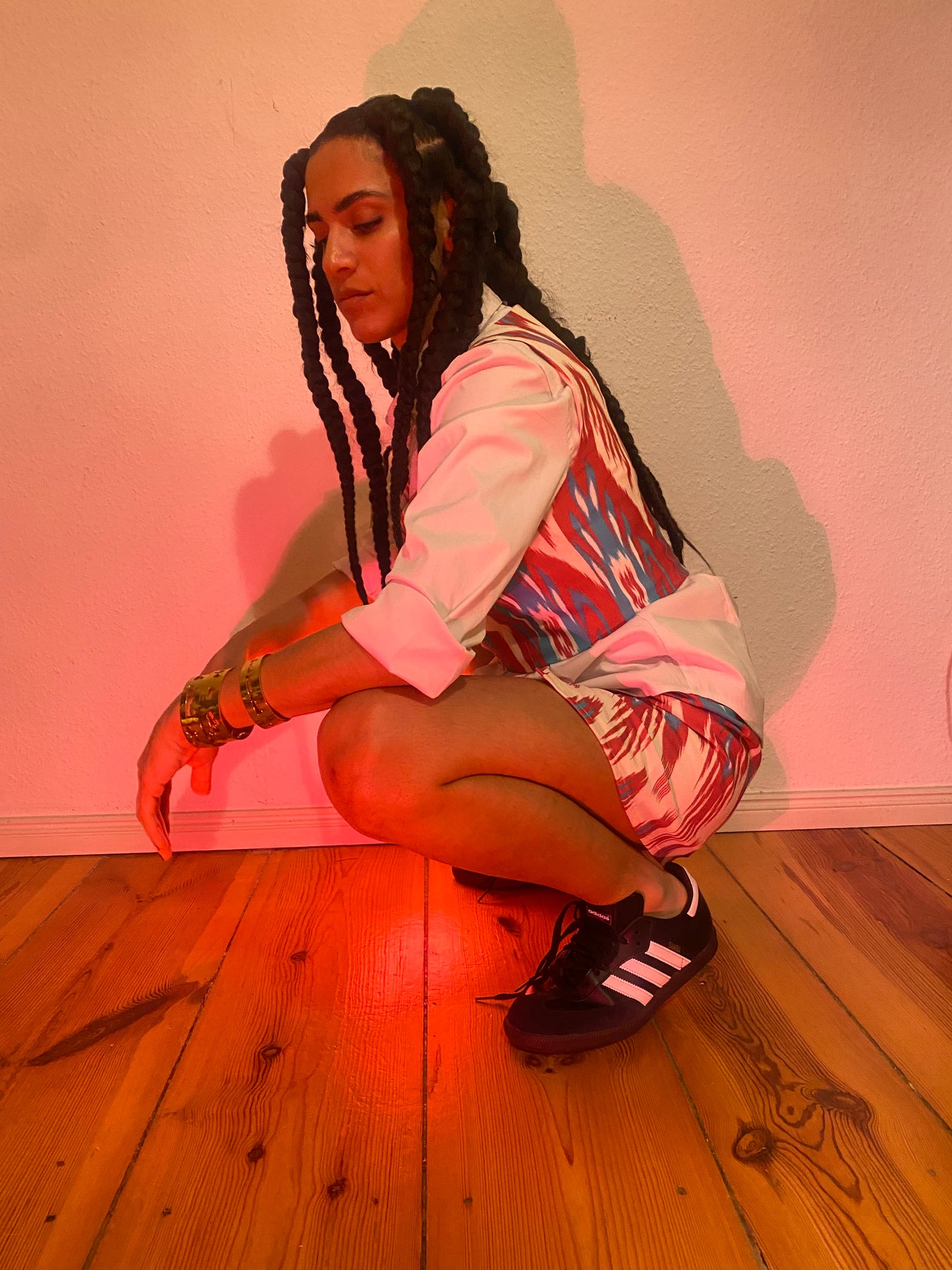 A profile shot of a woman squatting in Adidas Sambas and an all Uzbeki ikat set outfit.