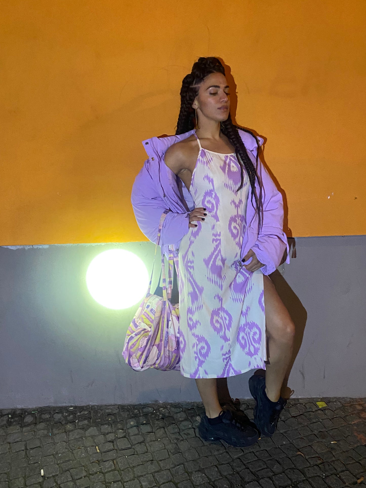 A woman strikes a pose on a night street showing the curve of her back in a white and lavender adras dress.