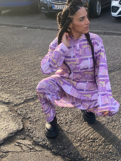 A woman with braids squatting in a peran tunban made of 100 Afghani fabric with cars in the background.