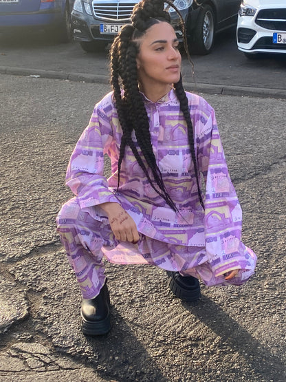 A woman with braids squatting in a peran tunban made of 100 Afghani fabric and smiling to the side.