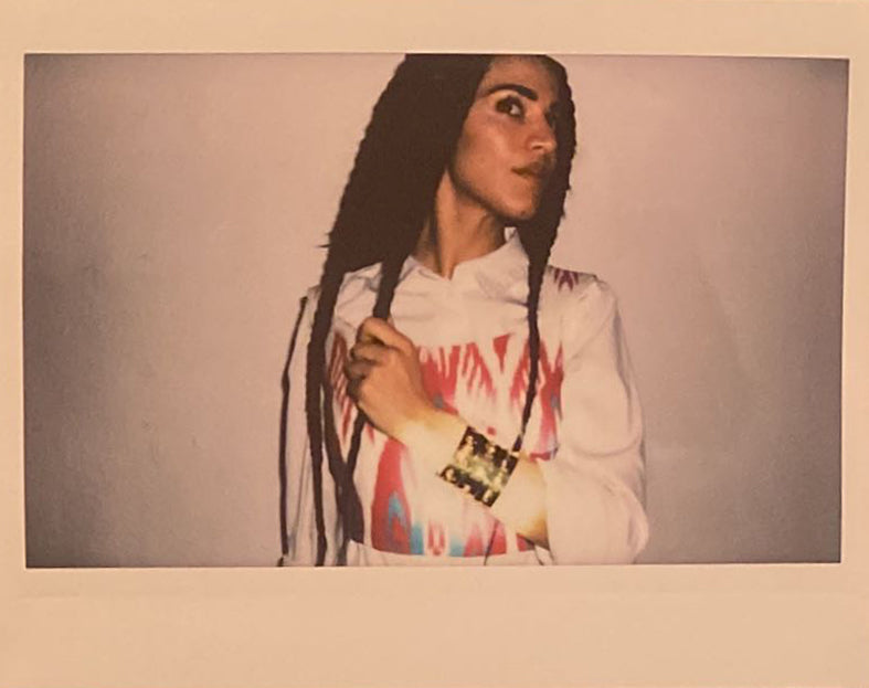 Close up polaroid of a woman with braids, an Uzbeki ikat top, white collared shirt and 3 gold bangles.